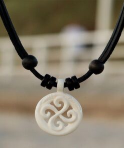 Frau trägt eine Koru-Halskette, ein maorisches Symbol, am Strand. Der Koru symbolisiert Wachstum und Harmonie.